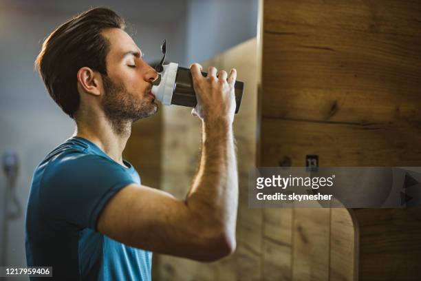 vista del perfil del hombre atlético bebiendo agua en el vestuario de un gimnasio. - vestuario entre bastidores fotografías e imágenes de stock