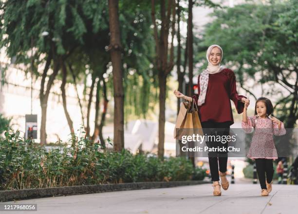 young asian malay mother carrying shopping bags and holding daughter's hand while walking on the street - malay hijab stock pictures, royalty-free photos & images