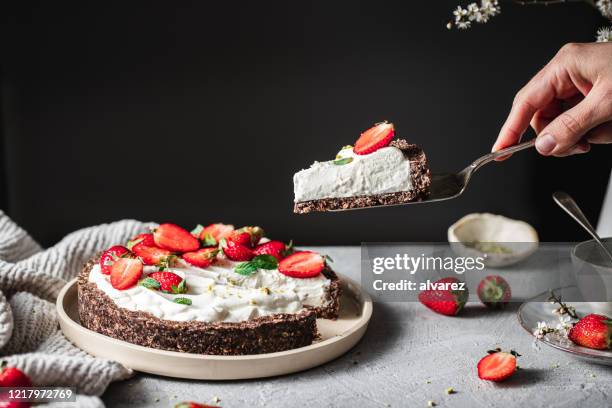 vrouw die een gedeelte van een yoghurtaardbeitaart neemt - spatel stockfoto's en -beelden