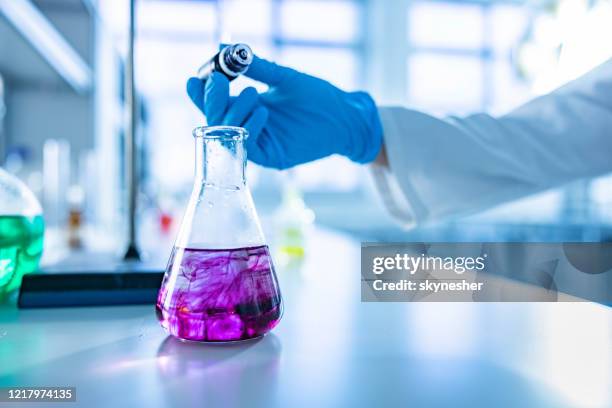 close up of unrecognizable scientist pouring purple paint into a beaker. - glass beaker stock pictures, royalty-free photos & images