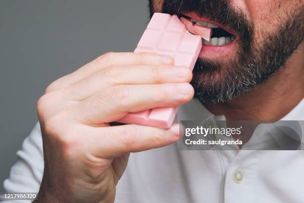 bearded man eating a strawberry flavored chocolate bar - chocolate bar stock pictures, royalty-free photos & images