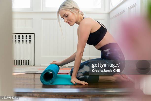 young woman unrolling yoga mat at home - rolling stock-fotos und bilder