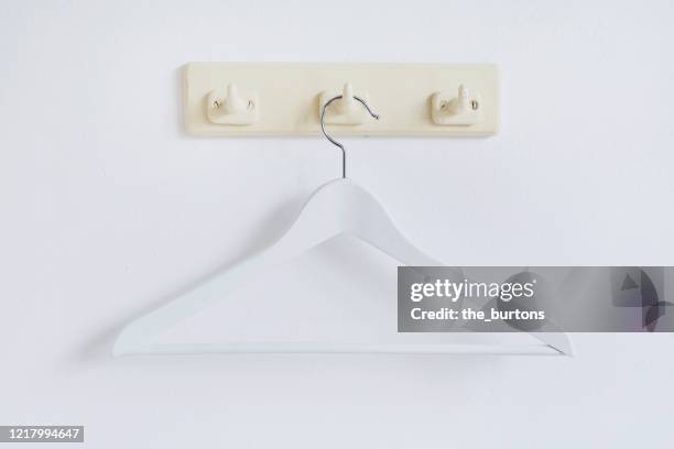 still life of a white coat hanger hanging at coat hook - kleiderbügel stock-fotos und bilder