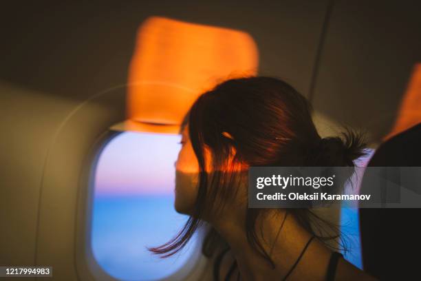portrait of young woman in plane illuminated with sunset light - 飛行機　窓 ストックフォトと画像