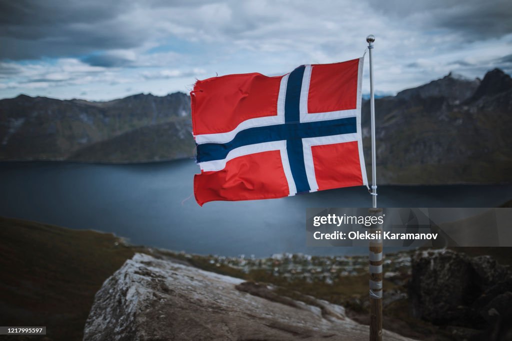 Norway, Senja, Norwegian flag with fjord and mountains in background