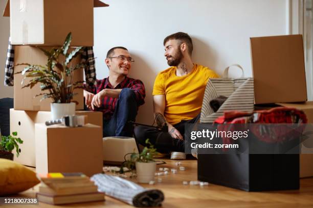 gay couple sitting on the floor tired of unpacking boxes - gay couple new house stock pictures, royalty-free photos & images