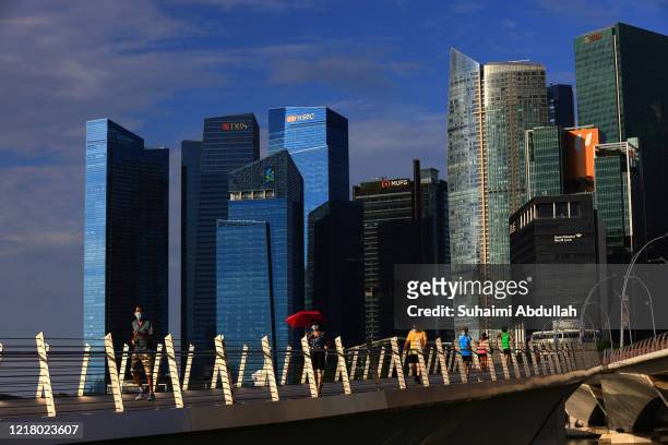 People wearing protective masks walk along the Jubilee Bridge at the Marina Bay waterfront on June 7, 2020 in Singapore. From June 2, Singapore...
