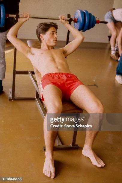 American actor Rob Lowe, dressed only in shorts, as he lifts weights during the filming 'The Hotel New Hampshire' , Canada, 1983.