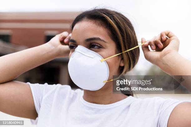 mujer adulta media poniéndose máscara facial n95 - mascarilla n95 fotografías e imágenes de stock