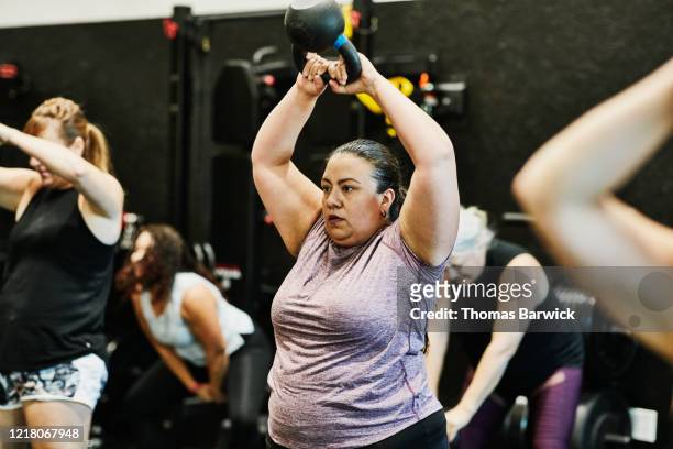 woman doing kettlebell swings while working out during class in gym - effort stock pictures, royalty-free photos & images