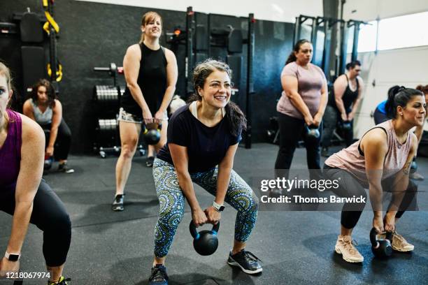 smiling woman doing kettlebell swings while working out during class in gym - exercise class fotografías e imágenes de stock