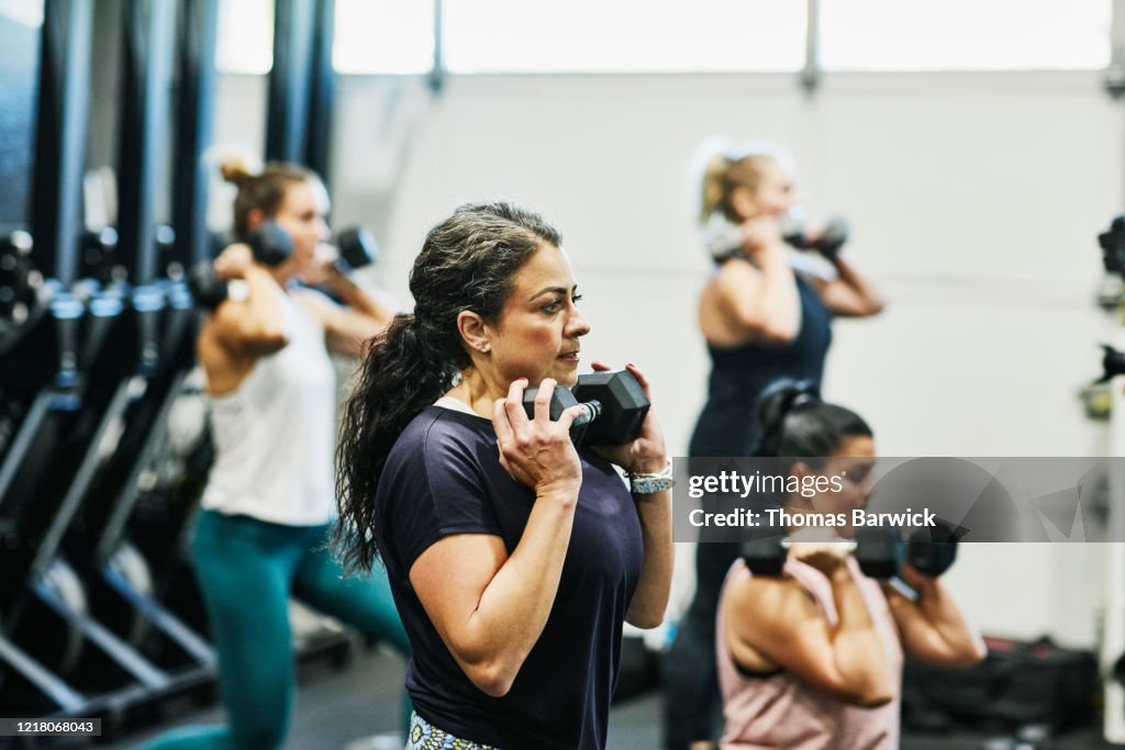 Woman doing dumbbell squats during fitness class in gym