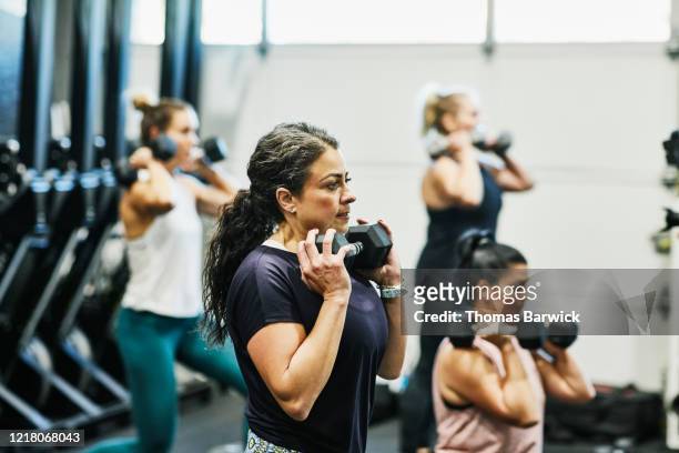 woman doing dumbbell squats during fitness class in gym - body building exercises stock pictures, royalty-free photos & images
