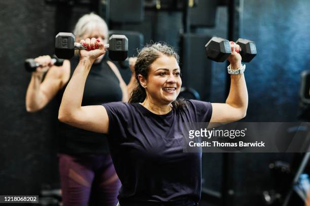 Smiling woman doing overhead dumbbell press during fitness class in gym