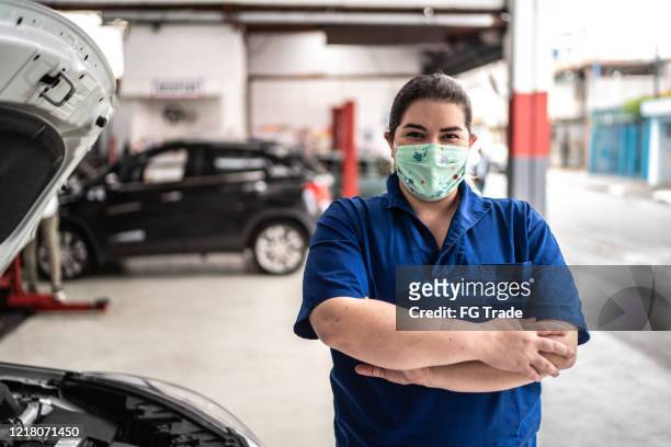 porträt der automechanikerin mit gesichtsmaske in der autowerkstatt - essenzielle berufe und dienstleistungen stock-fotos und bilder