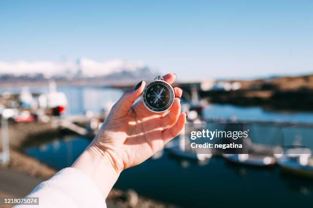 close-up of the hand of young woman holding compass in front of the  djupivogur dock and pier in iceland on the winter morning - compass city stockfoto's en -beelden