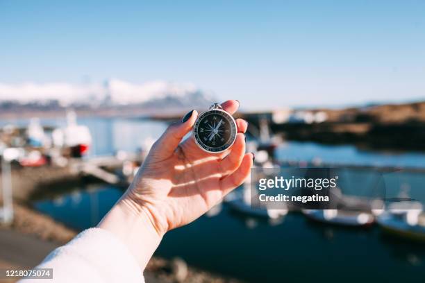 close-up of the hand of young woman holding compass in front of the  djupivogur dock and pier in iceland on the winter morning - compass city stock pictures, royalty-free photos & images