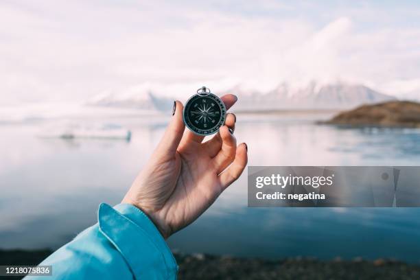 close-up of the hand of a young woman holding a compass with fingers in front of the glacier lagoon in iceland on a winter morning - compass city stockfoto's en -beelden