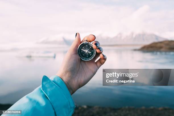 hand of a young woman holding a compass in front of the glacier lagoon in iceland on a winter evening - arrows landscapes stock pictures, royalty-free photos & images