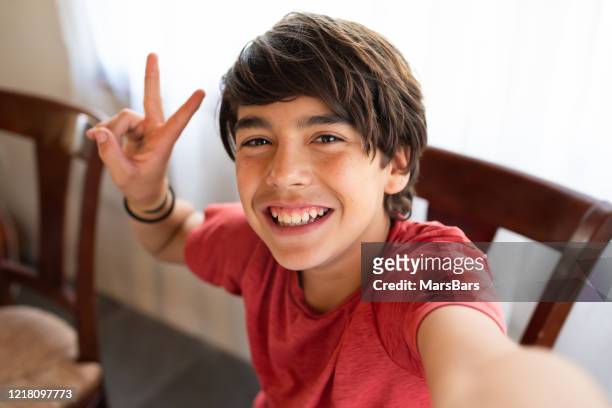 lindo latinx hispano niño sonriendo mientras se toma selfie en casa - gesto de victoria fotografías e imágenes de stock