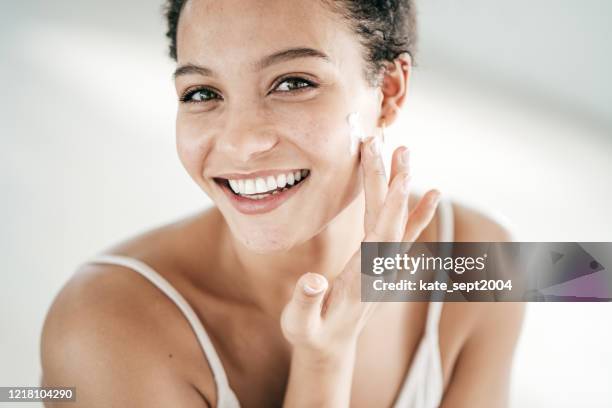 mujeres jóvenes sonrientes que aplican crema hidratante en su rostro - crema facial fotografías e imágenes de stock