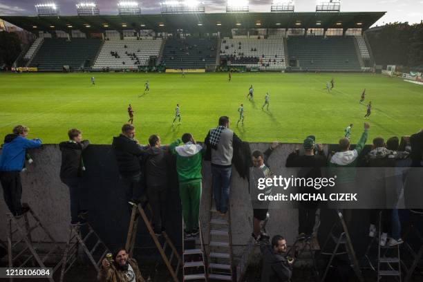 Bohemians' supporters follow the Czech First League football match between Bohemians 1905 and Sparta Praha from behind a wall, amid the new...