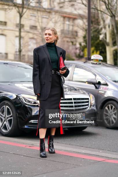 Guest wears a green turtleneck pullover, a black oversized blazer jacket, a belt, a black skirt, black and red shiny boots, a red leather bag,...