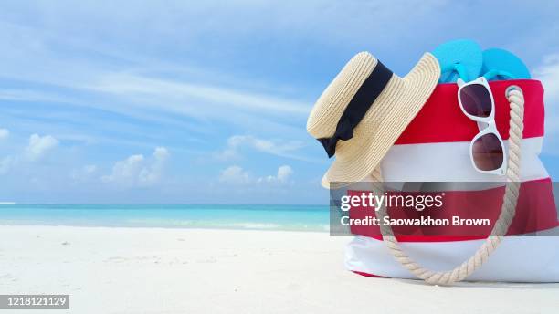 tourism and travel tropical vacation concept, red white striped beach bag flip-flops glasses and children toy on white sand beach. family vacation background - red white and blue beach stock pictures, royalty-free photos & images