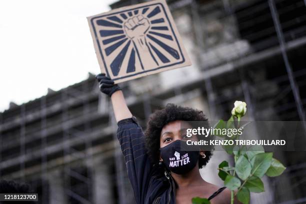 Woman wears a protective face mask on which is written 'Black Lives Matter', and holds a white rose and a placard depicting a fist, during an...