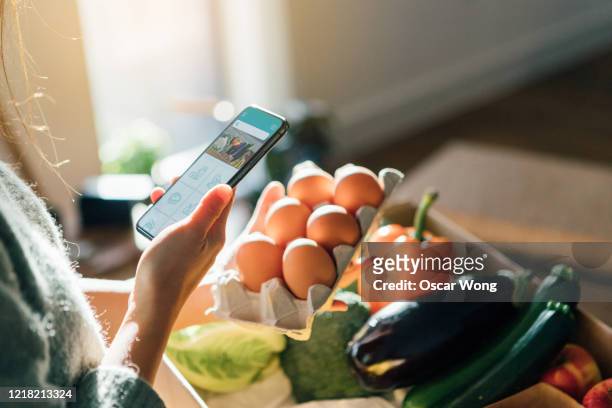 young woman ordering groceries online with smartphone - woman cooking phone stock-fotos und bilder