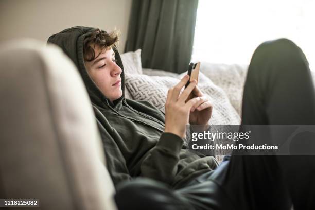 teenage boy using smartphone at home - online messaging photos et images de collection