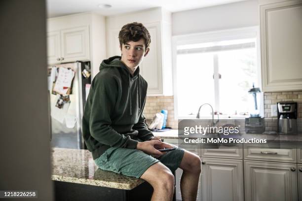 teenage boy looking out window at home - boy kitchen stockfoto's en -beelden