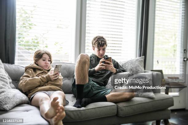 teenage siblings looking at smartphones and laughing - teen girl barefoot at home stock pictures, royalty-free photos & images