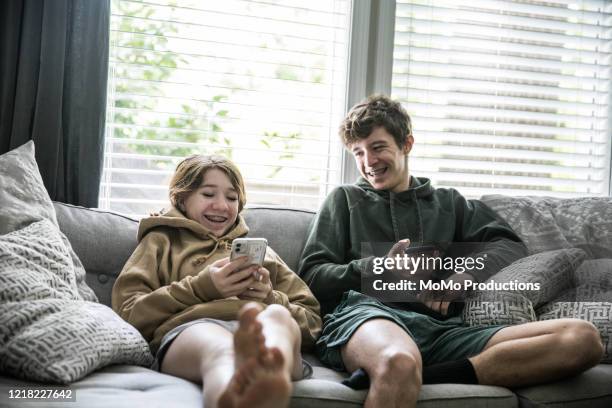 teenage siblings looking at smartphones and laughing - teen boy barefoot stock-fotos und bilder