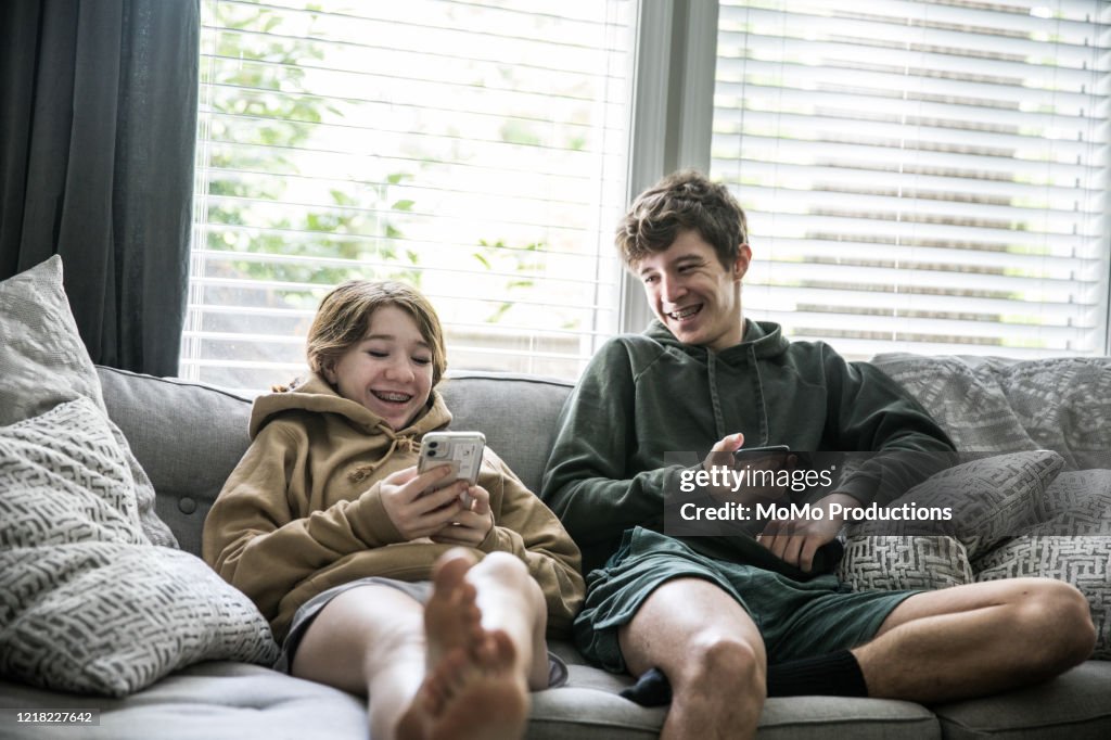 Teenage siblings looking at smartphones and laughing