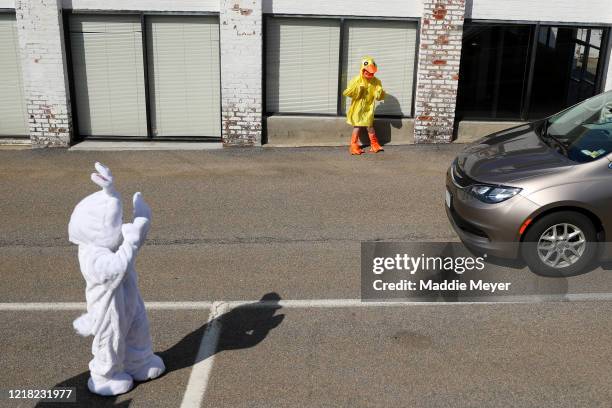 Boston Phillips dressed as a chick, and Landon Phillips dressed as the Easter Bunny, wave to cars during a drive-through Easter photo session at...