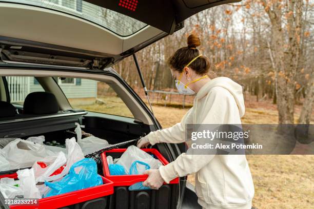 young woman unloading plastic reusable bins filled with groceries from the car's trunk to be delivered. - alex potemkin coronavirus stock pictures, royalty-free photos & images