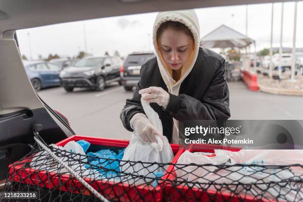 young woman, a courrier, is loading a car with groceries packed for delivery during a covid-19 pandemic. - alex potemkin coronavirus stock pictures, royalty-free photos & images