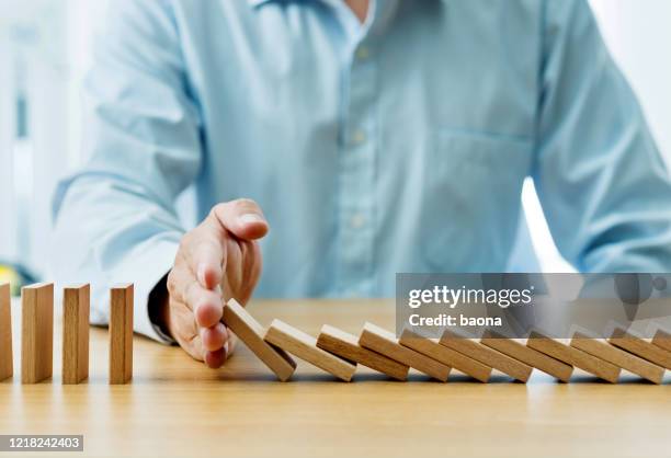 businessman hand stopping falling blocks on table - crisis leadership stock pictures, royalty-free photos & images