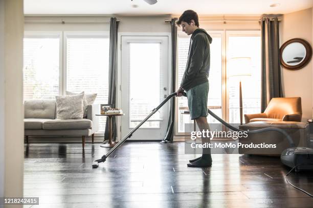 teenage boy vacuuming living room at home - teen boy shorts stock pictures, royalty-free photos & images