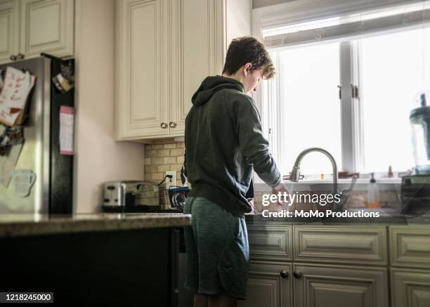 teenage boy doing dishes in kitchen - teen boy shorts imagens e fotografias de stock