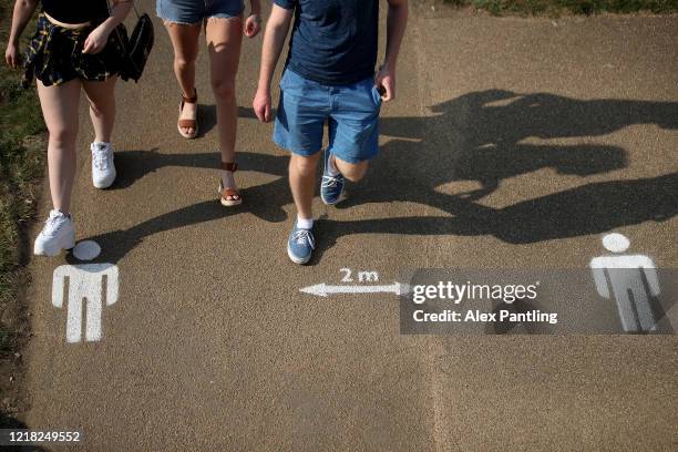 People walk past the social distancing markings on the ground at Queen Elizabeth Olympic Park on April 11, 2020 in London, England. Public Easter...