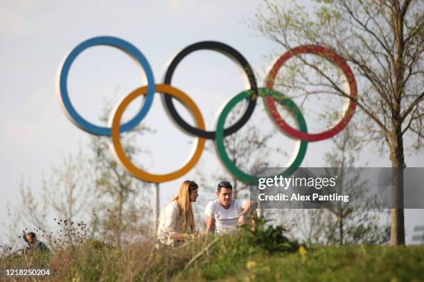 People sit and enjoy the sunshine infront of the Olympic Rings at Queen Elizabeth Olympic Park on April 11, 2020 in London, England. Public Easter...