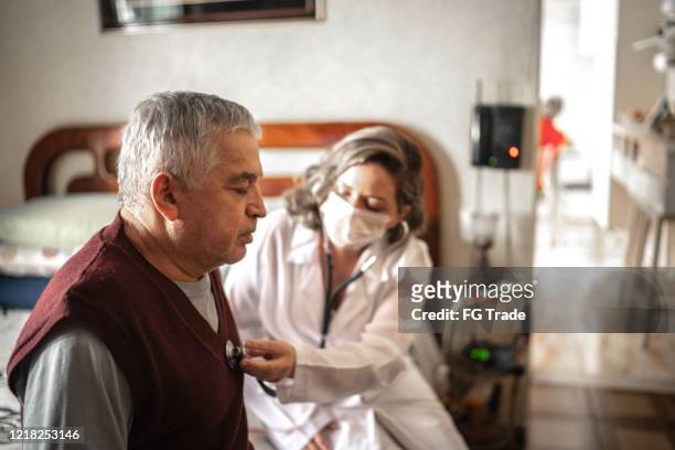 visitante de salud que escucha los latidos del corazón del hombre mayor durante la visita a casa - illness fotografías e imágenes de stock