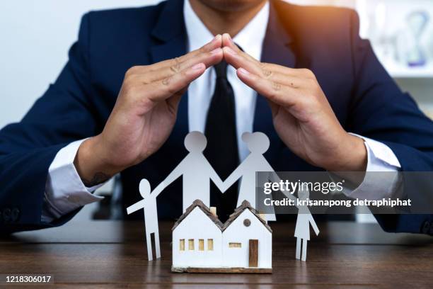 businessman protecting toy house by hands. professional insurer thinking about plans possible defense for building and family. property insurance concept - possible fotografías e imágenes de stock
