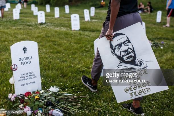 Person holds a placard with a portrait of George Floyd during a candlelight vigil at an installation created by Anna Barber and Connor Wright called...