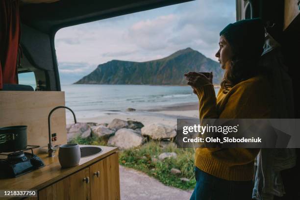 woman drinking tea in camper van with view on beach on lofoten island - camper van imagens e fotografias de stock