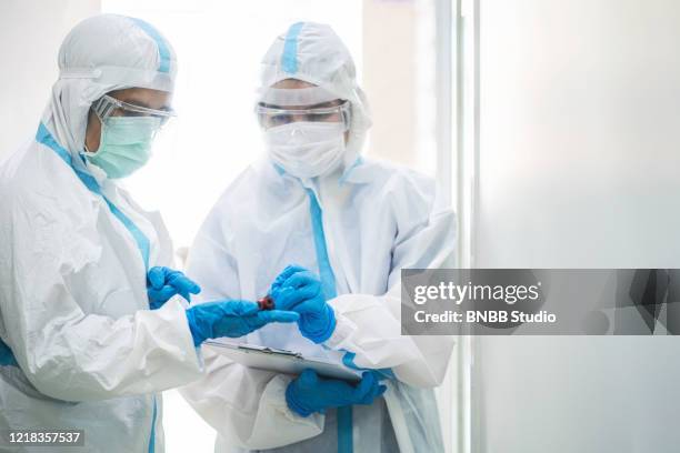 asian doctor in ppe medical suit holding coronavirus or covid-19 blood testing tube in quarantine room - infection prevention stockfoto's en -beelden