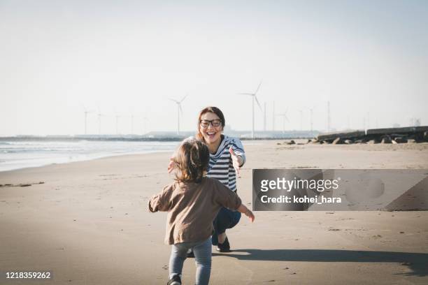 mutter und baby entspannt am strand in der nähe des windparks - fuel and power generation stock-fotos und bilder