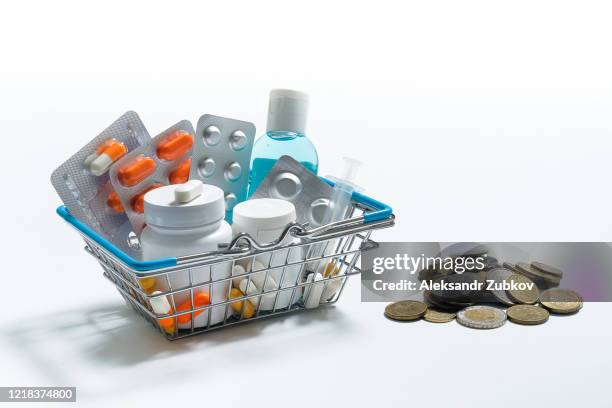 tablets and medications in the shopping cart on a white background. next to the coins of all countries of the world. - prescription drug costs stock pictures, royalty-free photos & images